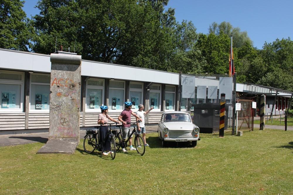 Drei Personen mit E-Bikes stehen vor der Grenzdokumentationsstätt Lübeck-Schlutup