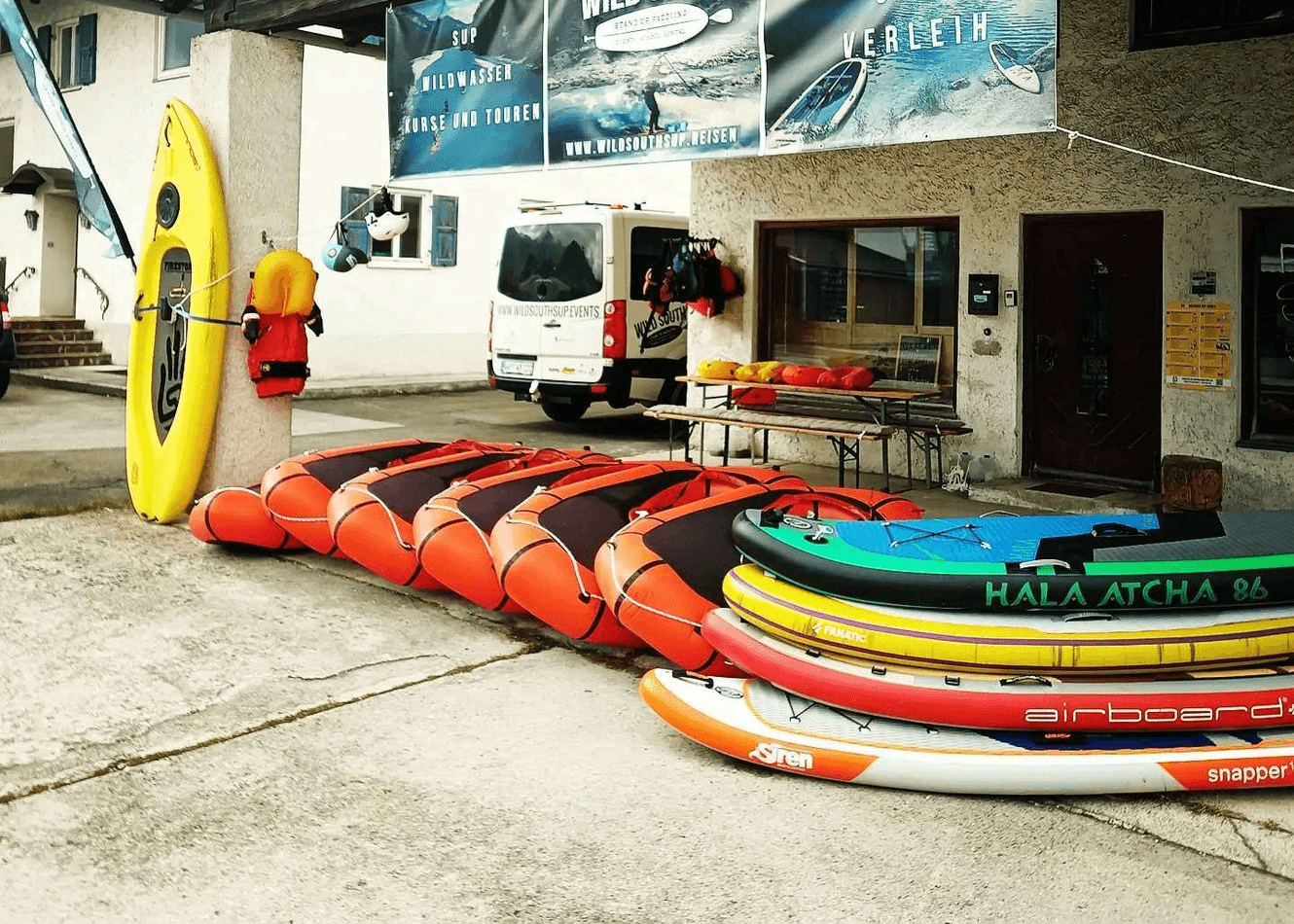 Mehrere Packrafts und SUP-Boards vor einem Verleih