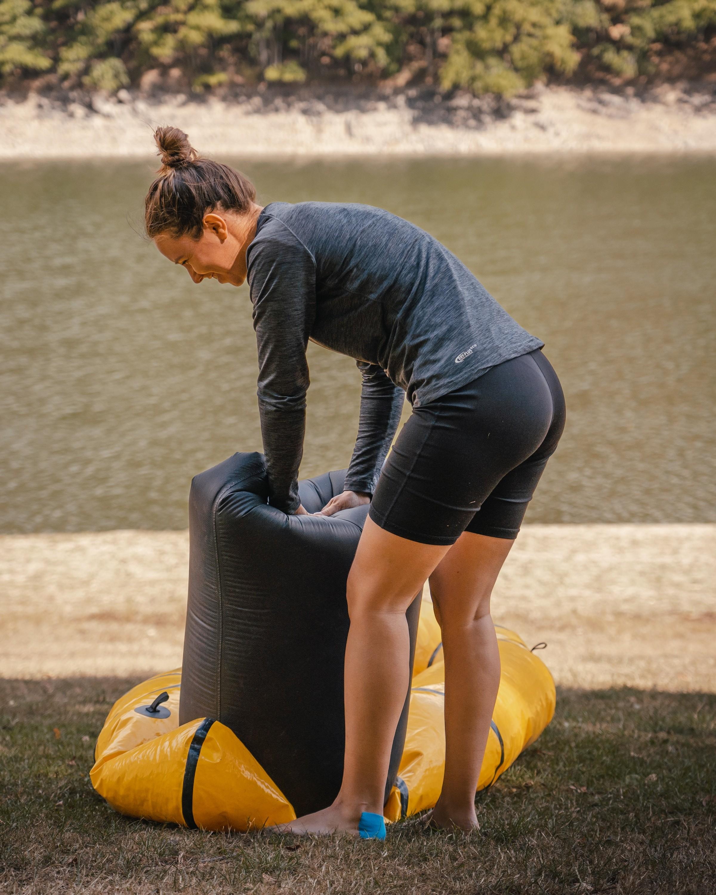 Eine Frau pumpt ein Packraft mithilfe eines Luftsacks auf