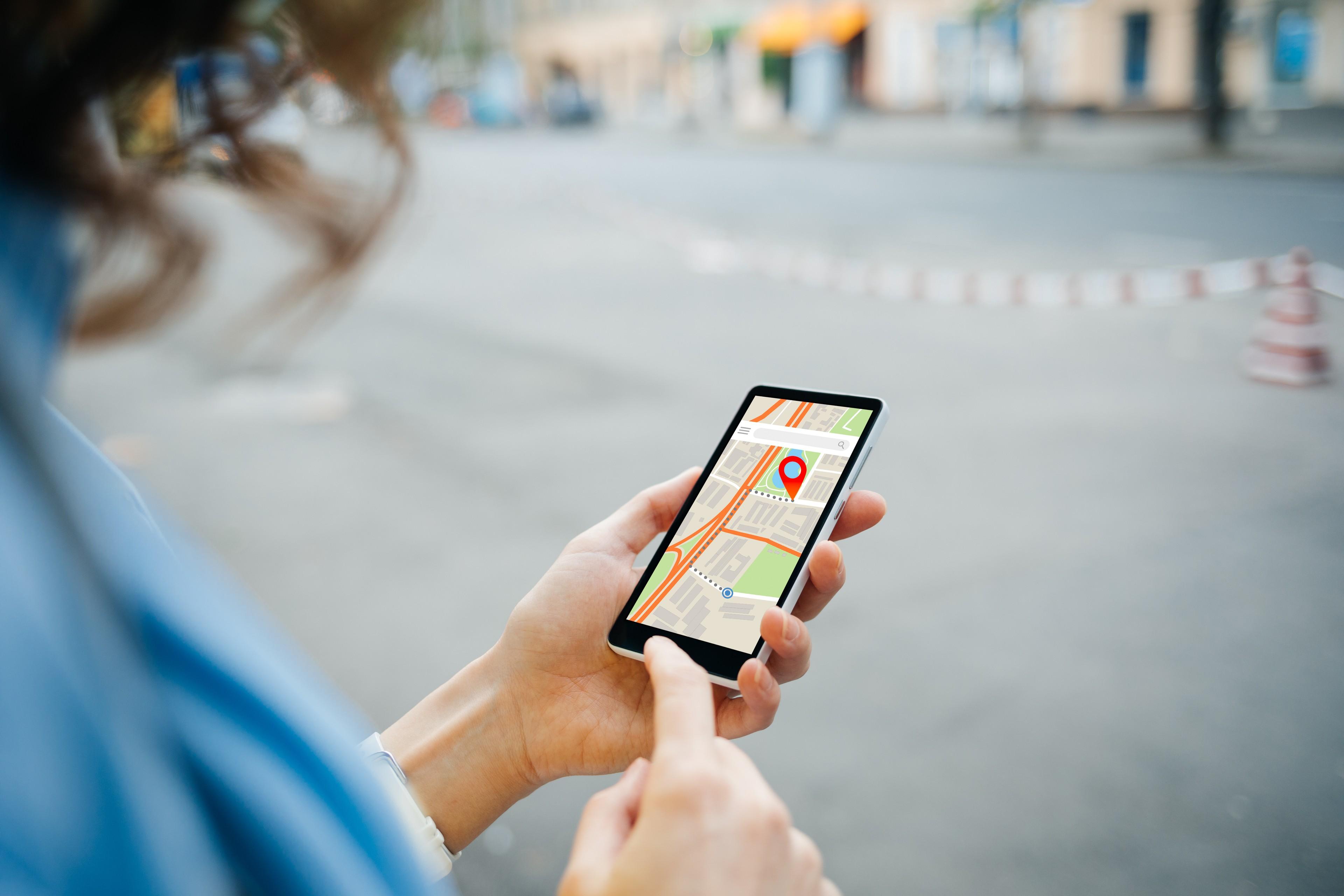 Eine Person hält ein Smartphone, auf dem ein Stadtplan mit Markierungen zu sehen ist