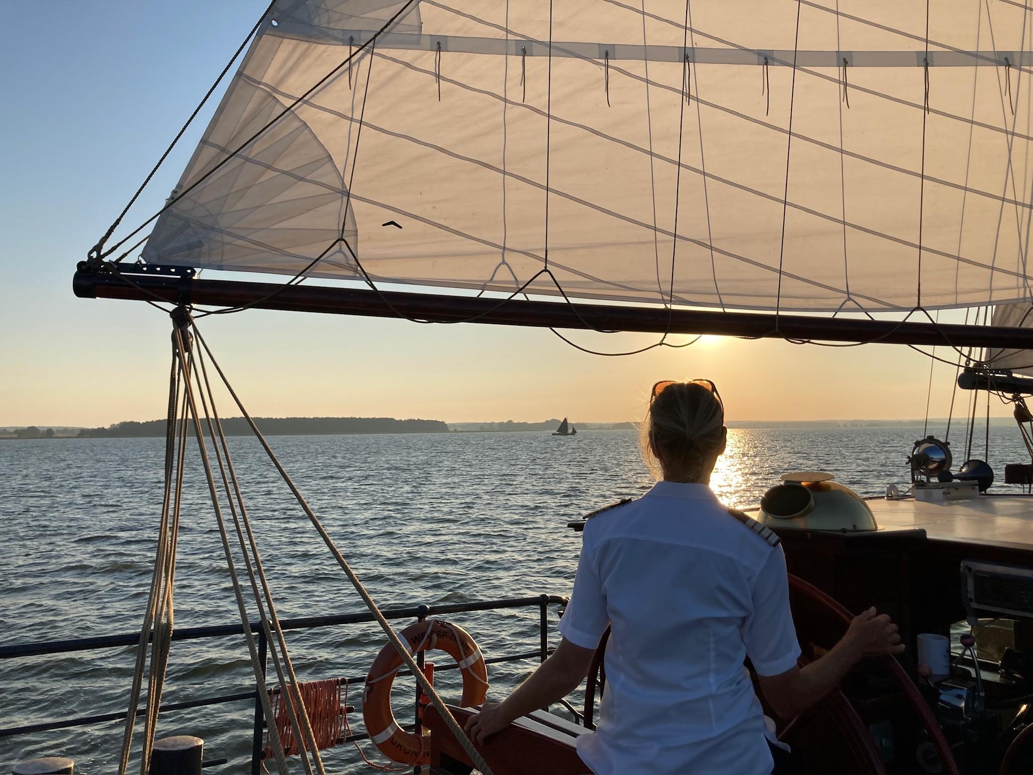 Eine Person schaut bei einem Segeltörn mit dem Schiff „Weisse Düne“ auf der Ostsee in den Sonnenuntergang