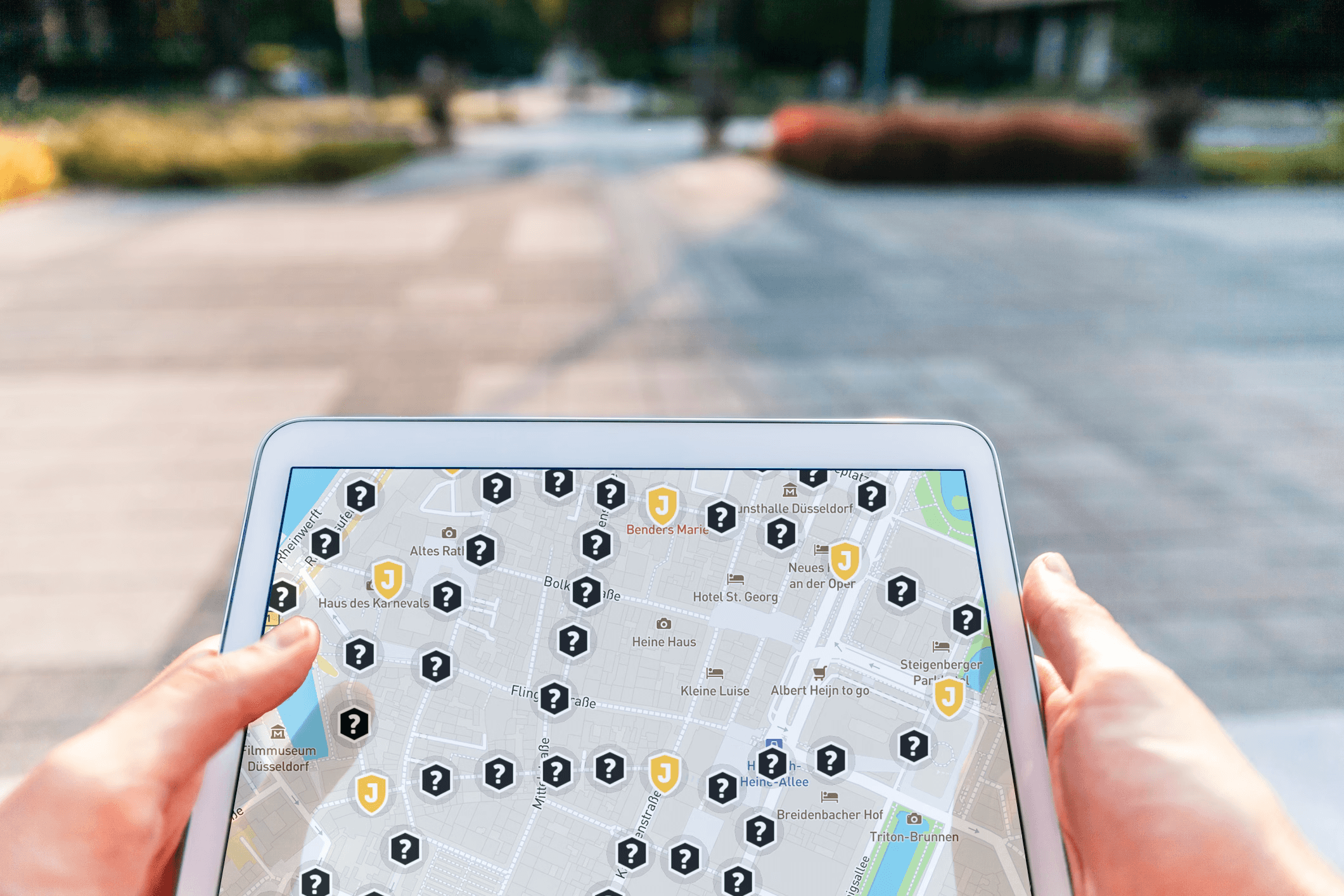 Hände halten ein Tablet, auf dem eine interaktive Stadtkarte mit Wegmarkierungen für eine digitale Schnitzeljagd zu sehen ist