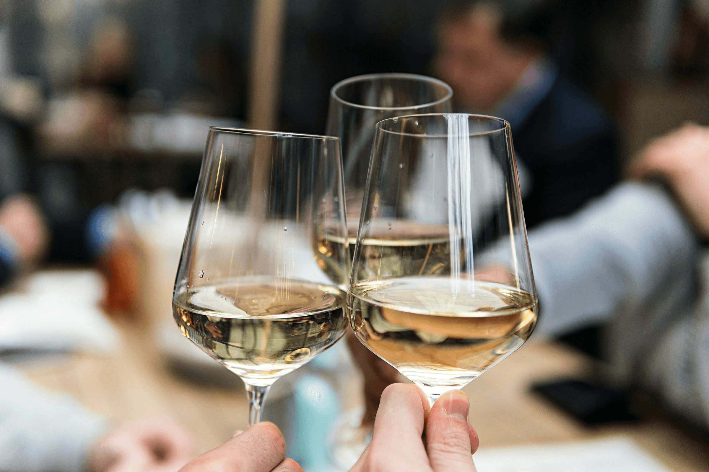 Drei erhobene Weißweingläser bei einer Weinprobe