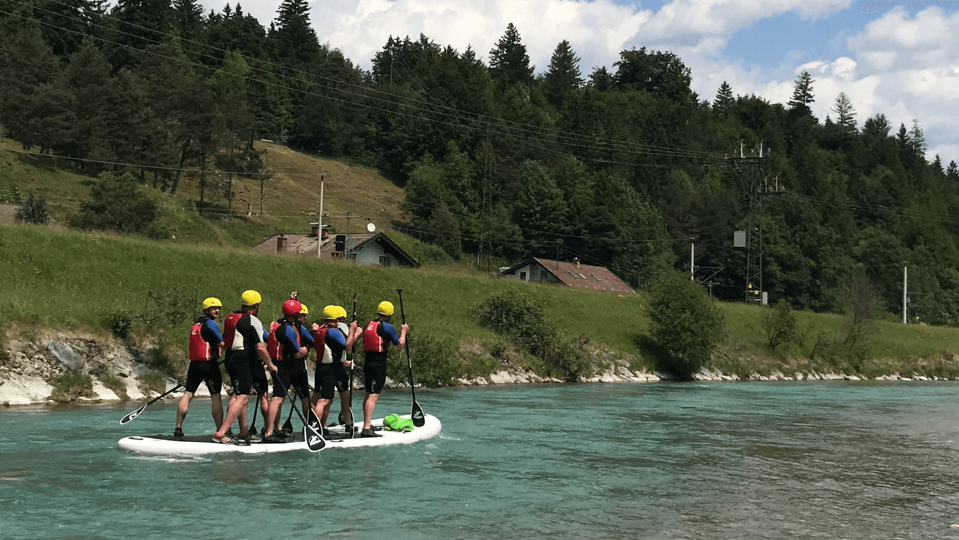 Eine Gruppe von Menschen befährt auf einem Maxi-SUP-Board einen Fluss