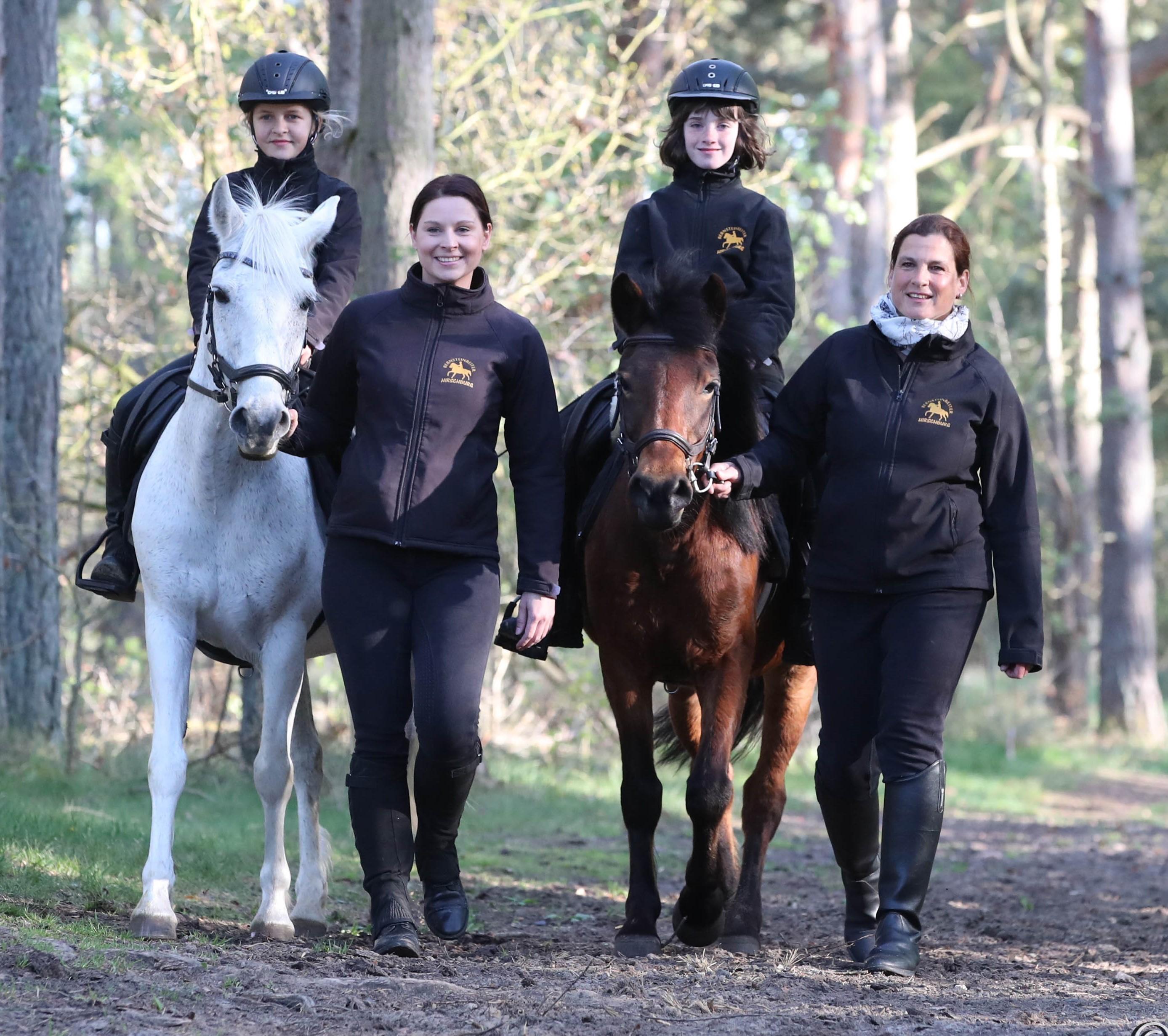 Zwei Mädchen sitzen auf Ponys, die von zwei Frauen geführt werden