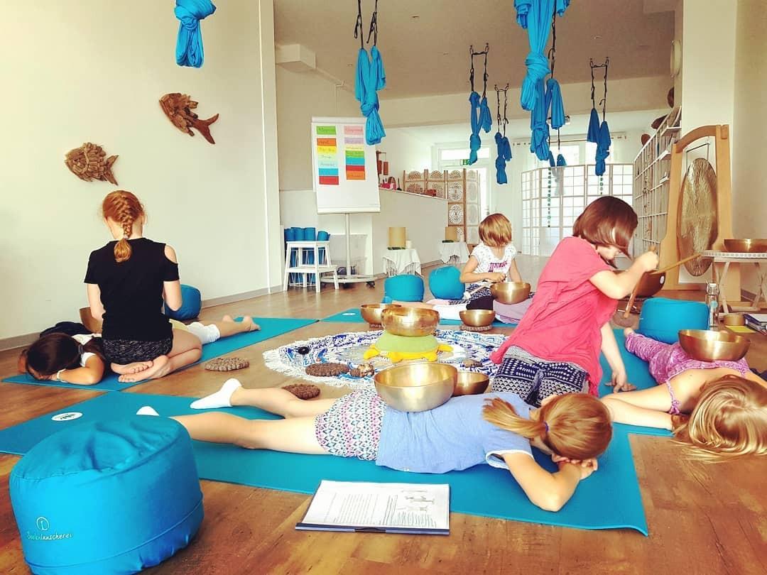 Kinder liegen in einem Raum auf Yoga-Matten und haben Klangschalen auf dem Rücken