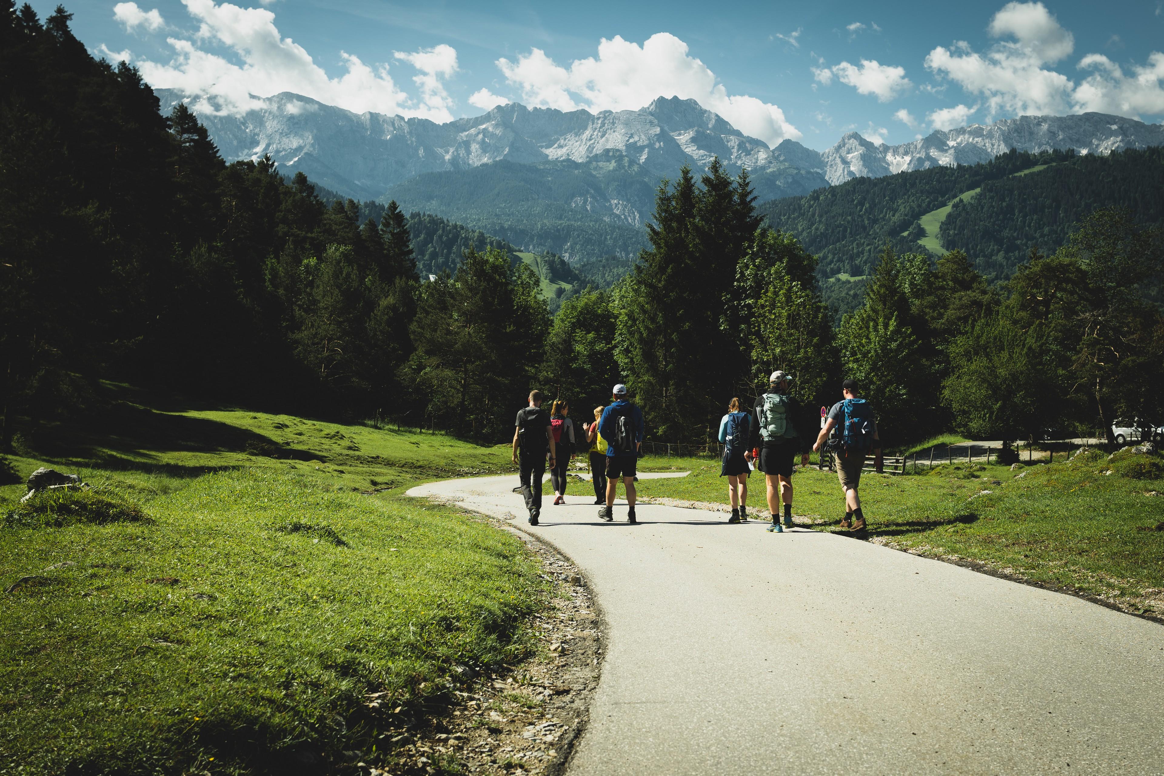 Eine Gruppe wandert auf einer Straße mit den Alpen im Hintergrund