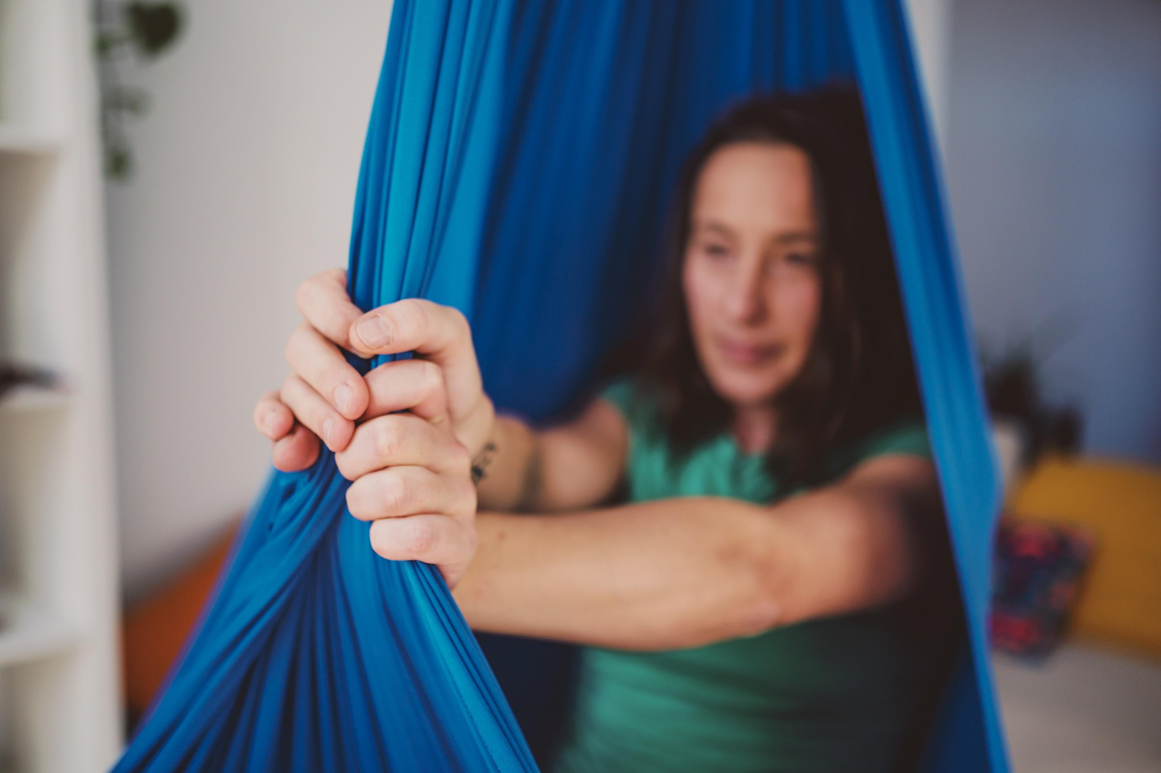 Eine Frau sitzt in einem Aerial-Yoga-Tuch und umfasst es mit beiden Händen