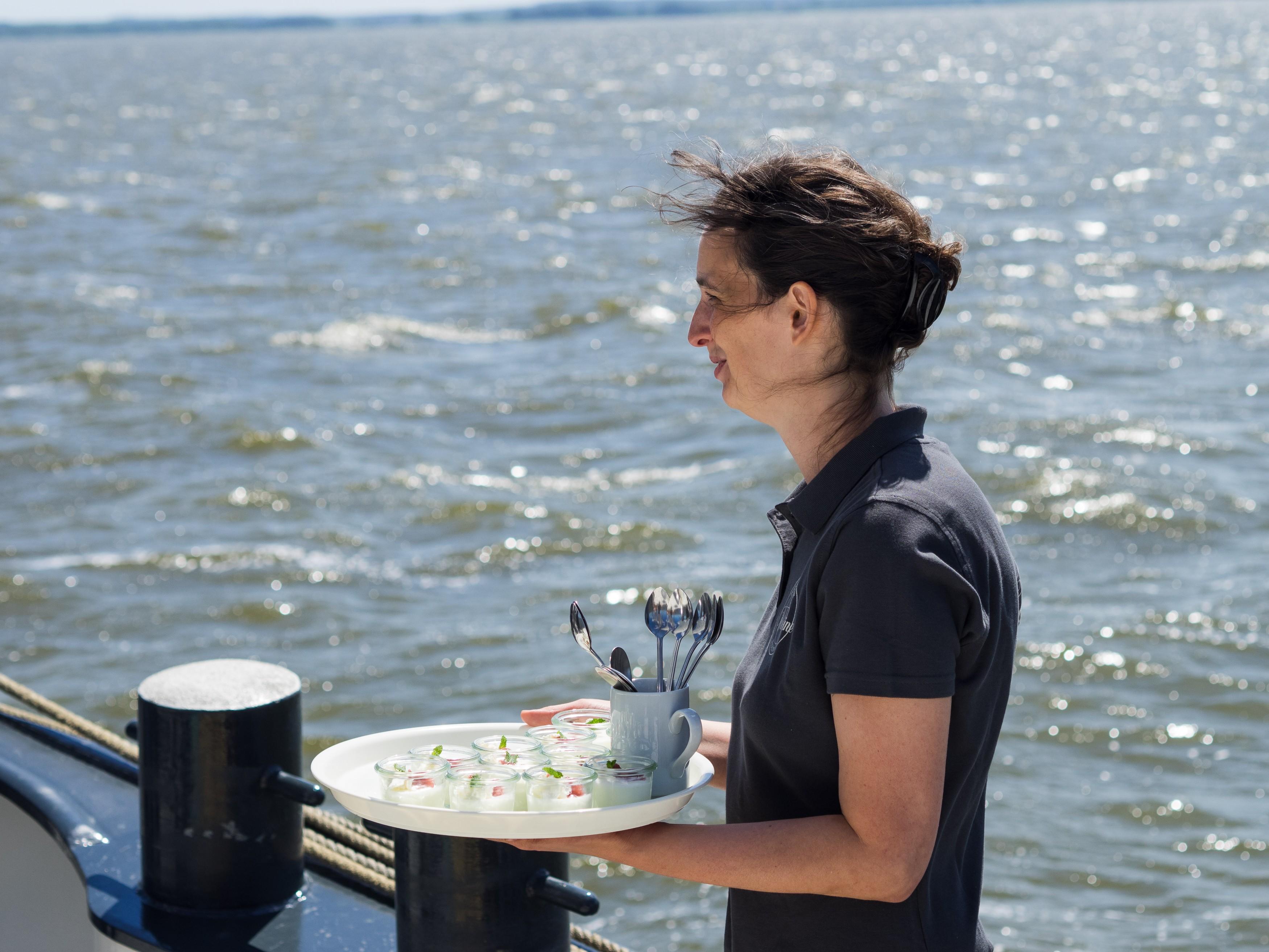 Eine Person bringt ein Tablett mit Speisen auf dem Segelschiff „Weisse Düne“