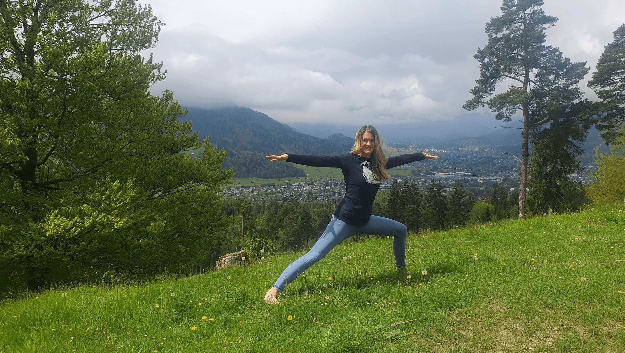 Eine Frau in Yoga-Pose auf einer Wiese in den Bergen