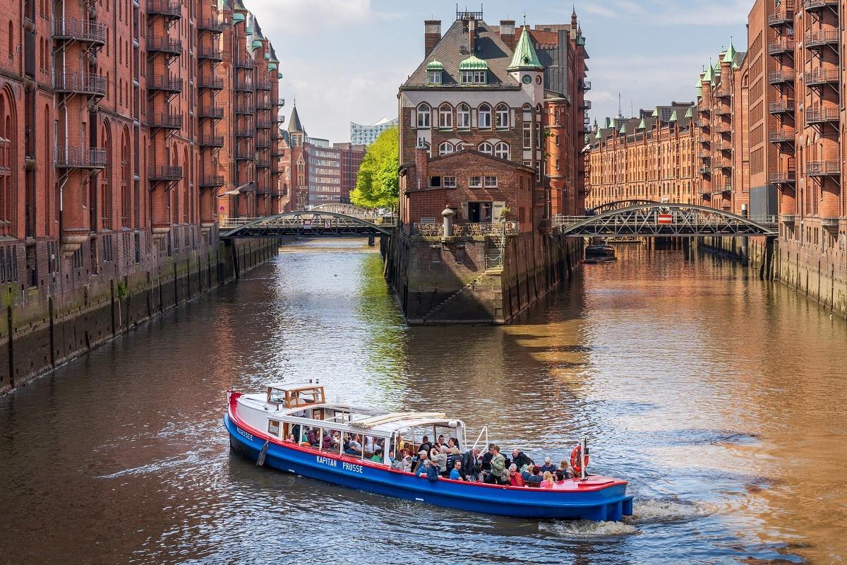 Eine blau-rote Barkasse der Schifffahrtsgesellschaft Kapitän Prüsse vor dem Wasserschloss in der Hamburger Speicherstadt