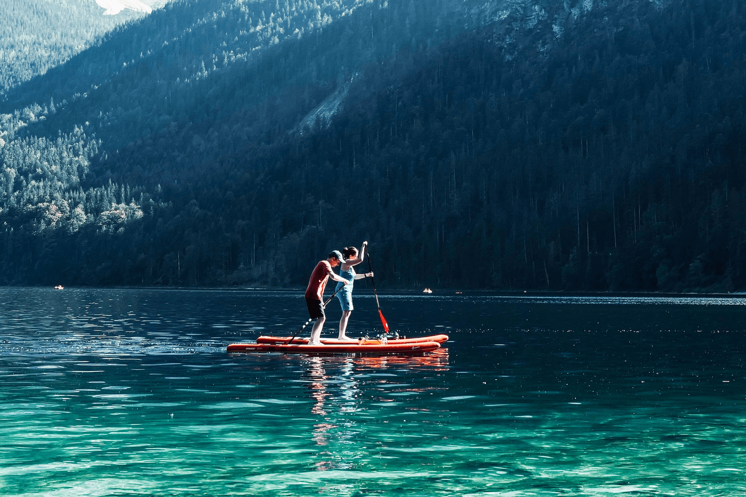 Zwei Personen auf SUP-Boards auf dem Eibsee mit bewaldeten Gebirgshängen im Hintergrund