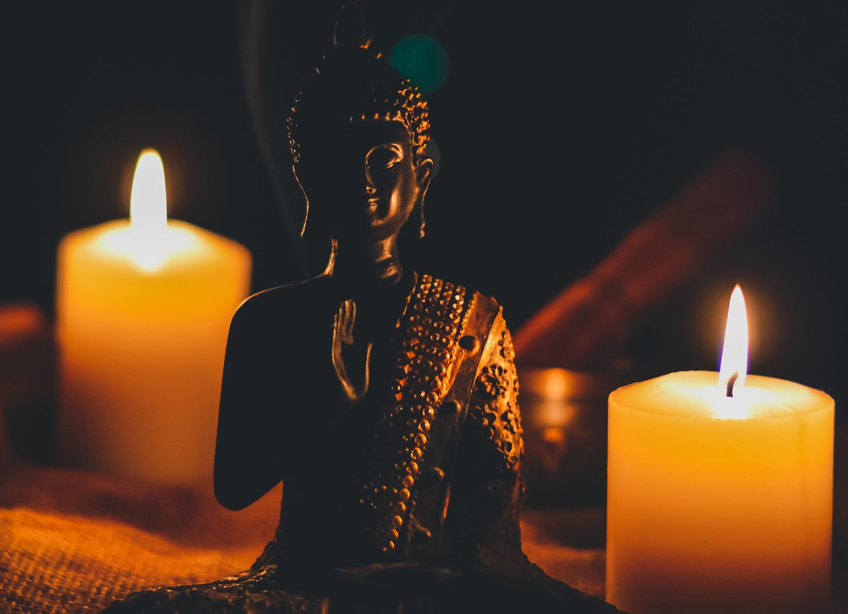 Eine Buddha-Figur steht zwischen zwei brennenden Kerzen