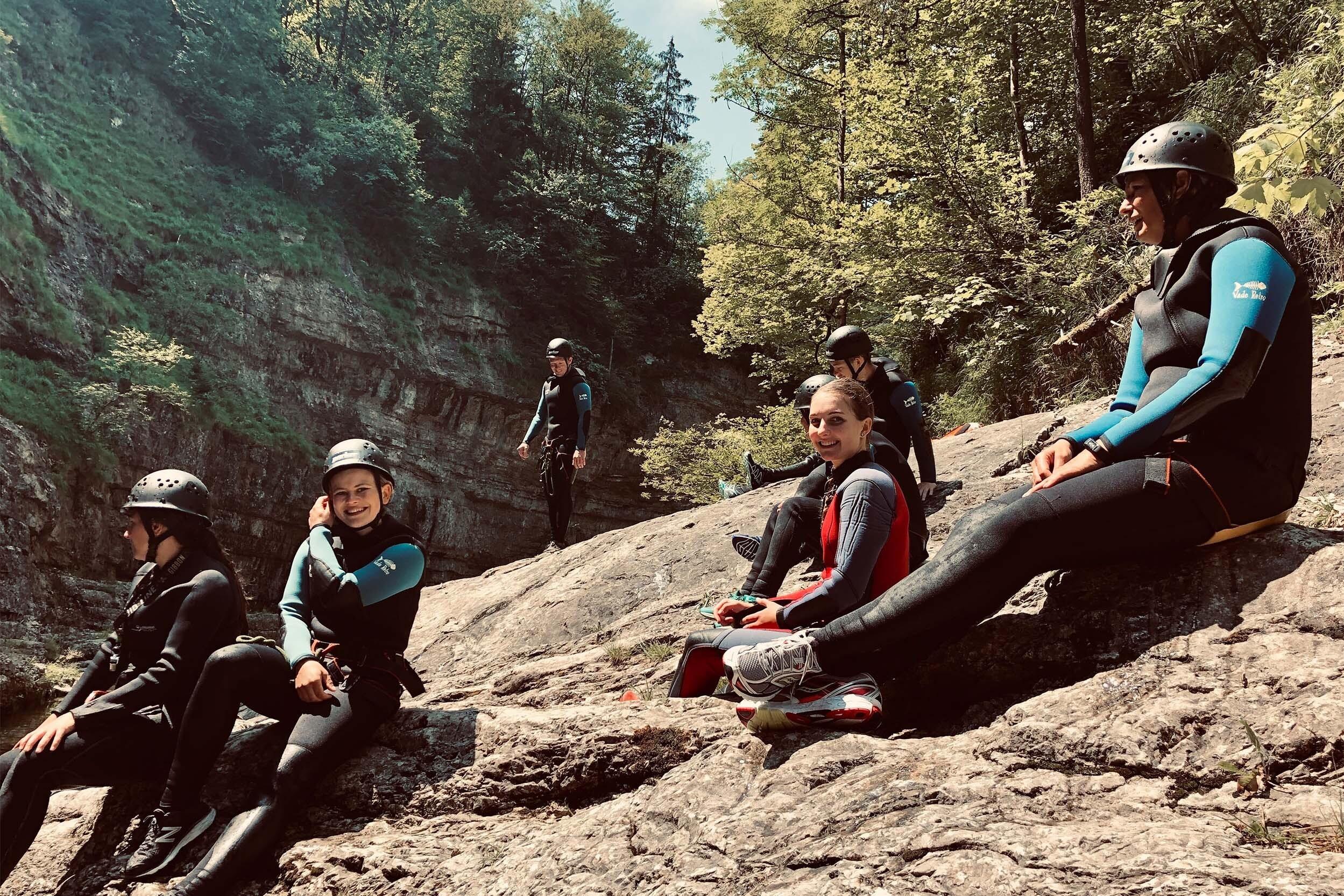 Eine Gruppe mit Helmen und Neoprenanzügen sitzt auf einem Felsen in den Bergen