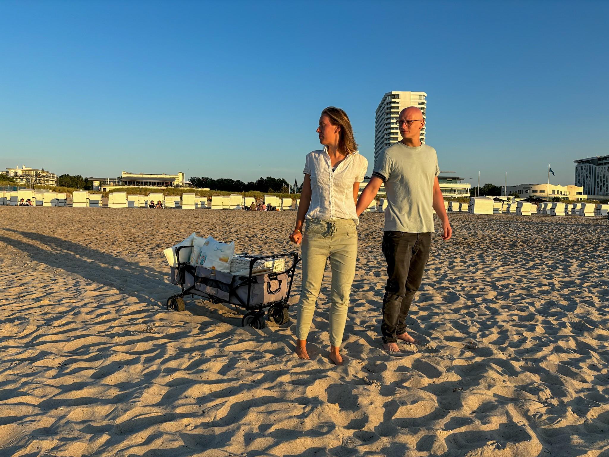 Zwei Personen ziehen einen Bollerwagen mit Picknick-Utensilien am Strand von Warnemünde