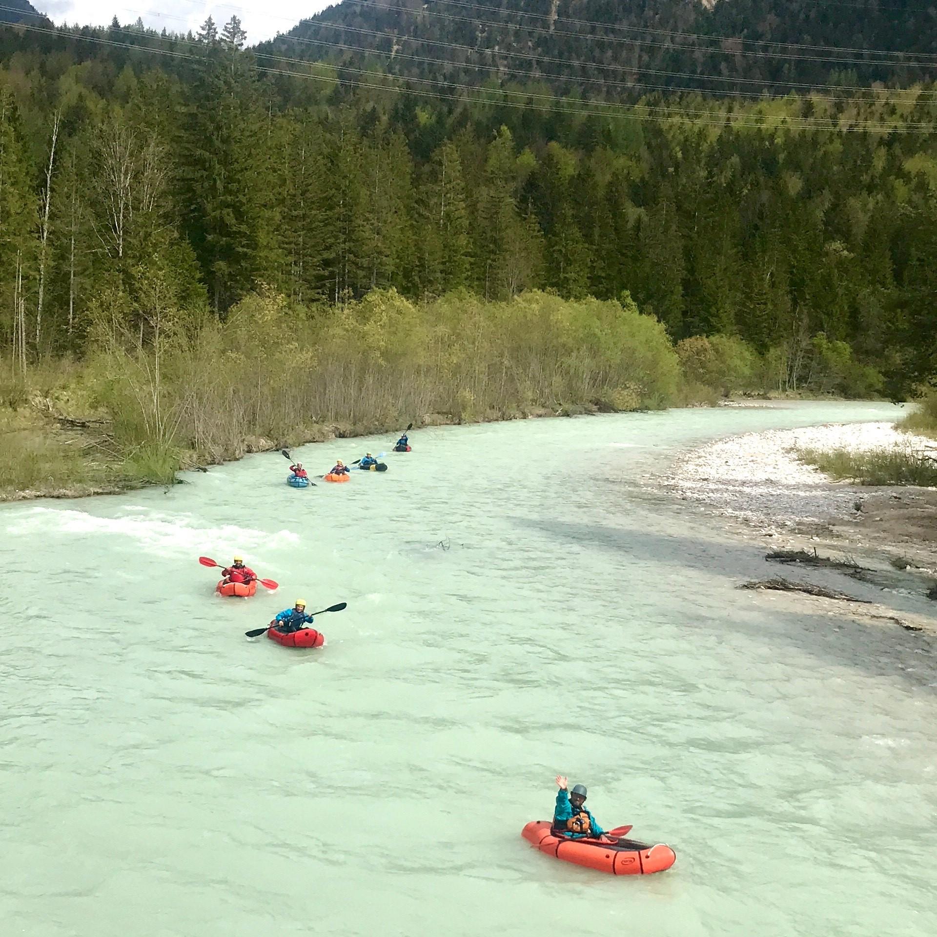 Eine Gruppe von Menschen befährt in Packrafts eine Flussbiegung in den Bergen