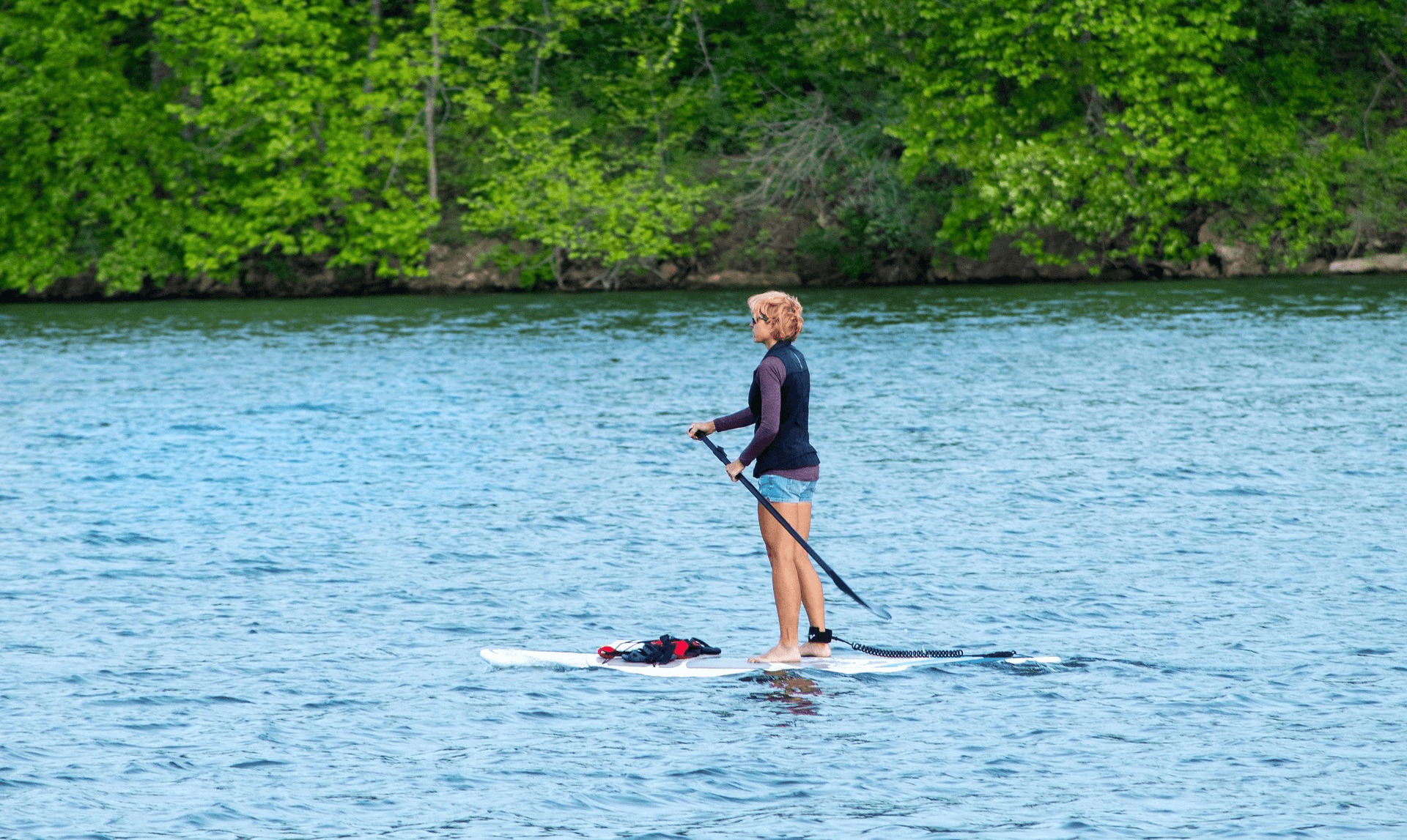 Eine Frau steht aufrecht auf einem SUP-Board auf einem Fluss mit Bäumen im Hintergrund