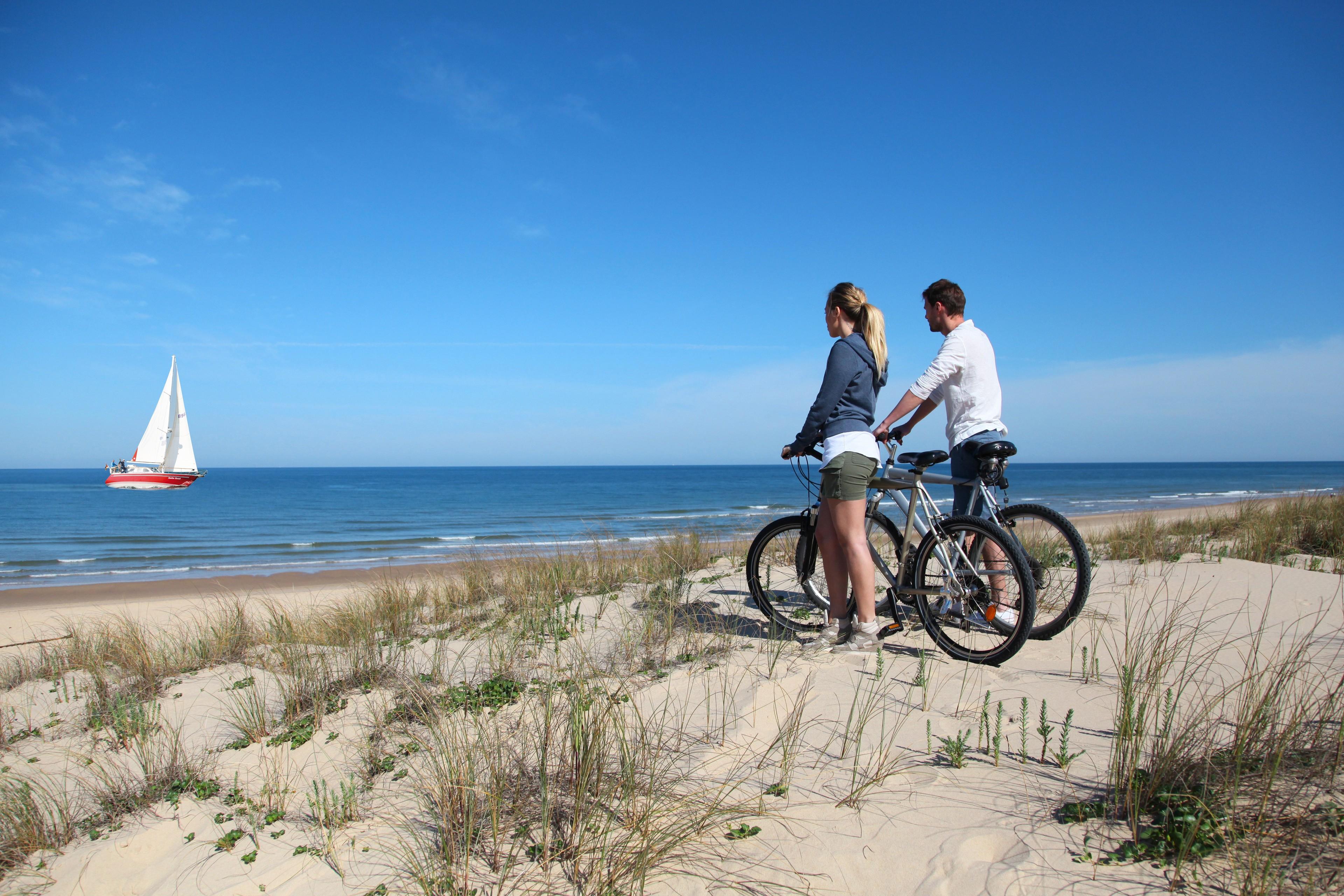 Zwei Personen stehen am Strand neben ihren Fahrrädern und betrachten ein Schiff