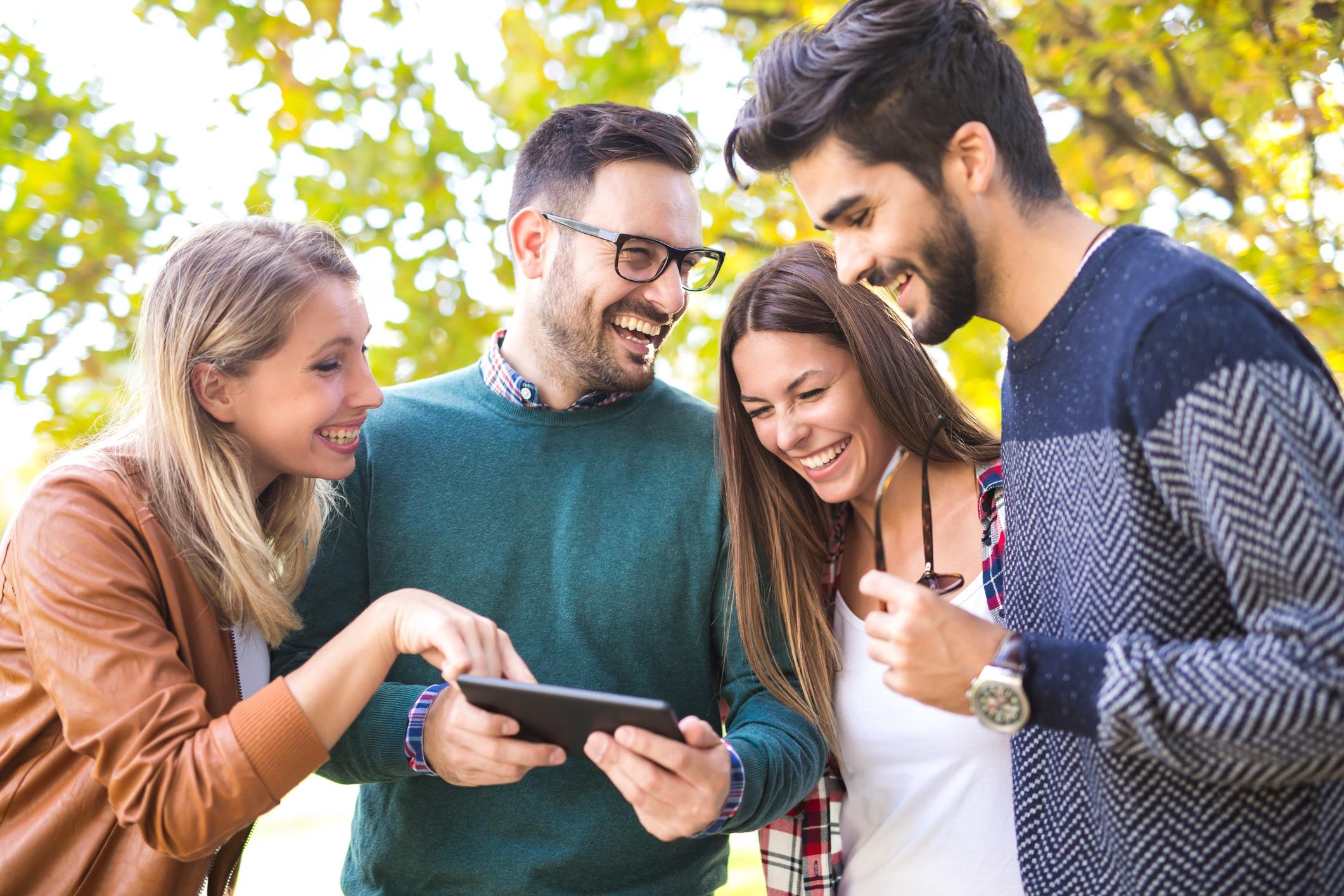 Eine Gruppe lachender, junger Menschen schaut während einer interaktiven Stadtrallye auf ein Tablet