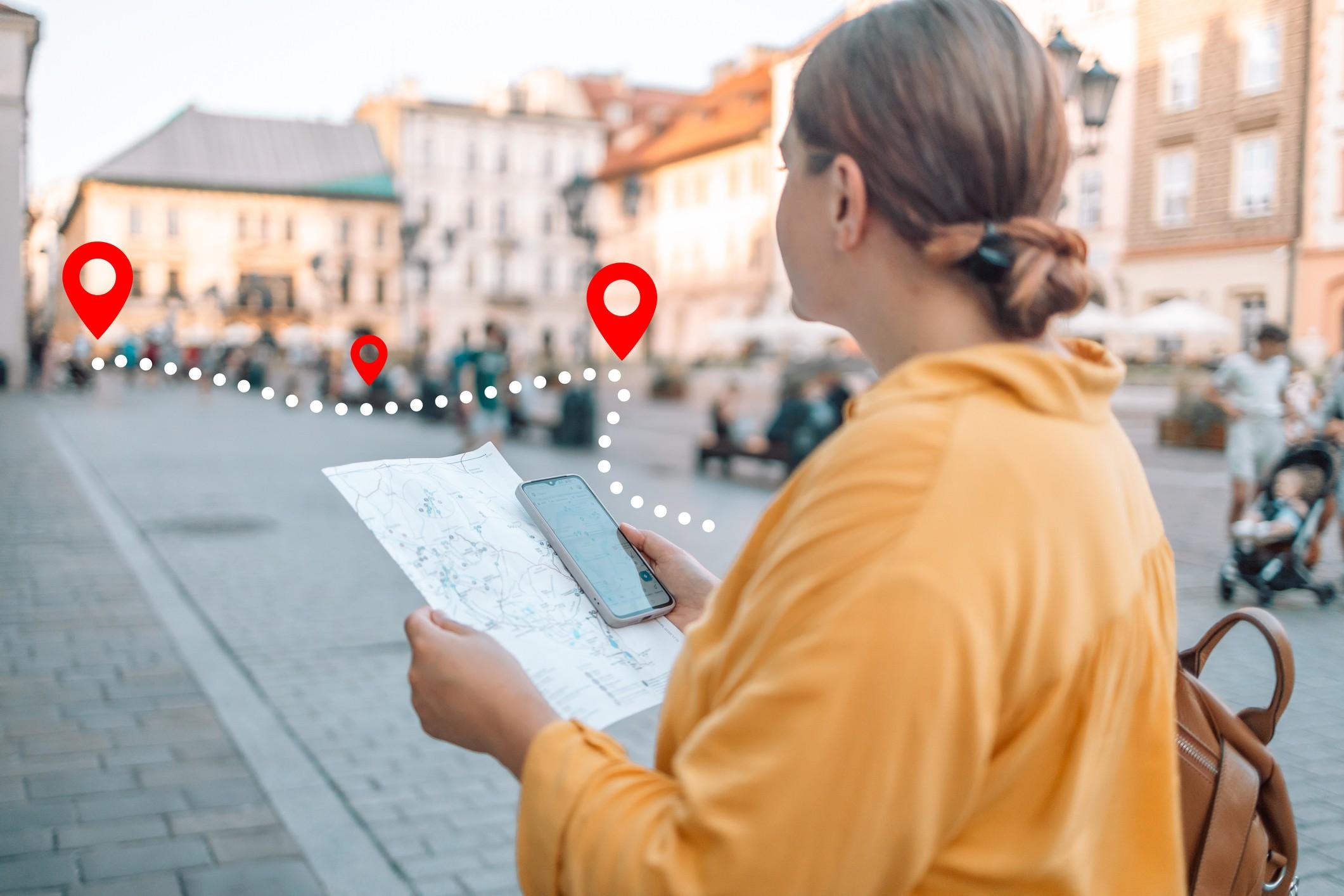 Eine Frau in einer Stadt hält beim Krimi-Geocaching ein Handy und eine Stadtkarte in den Händen