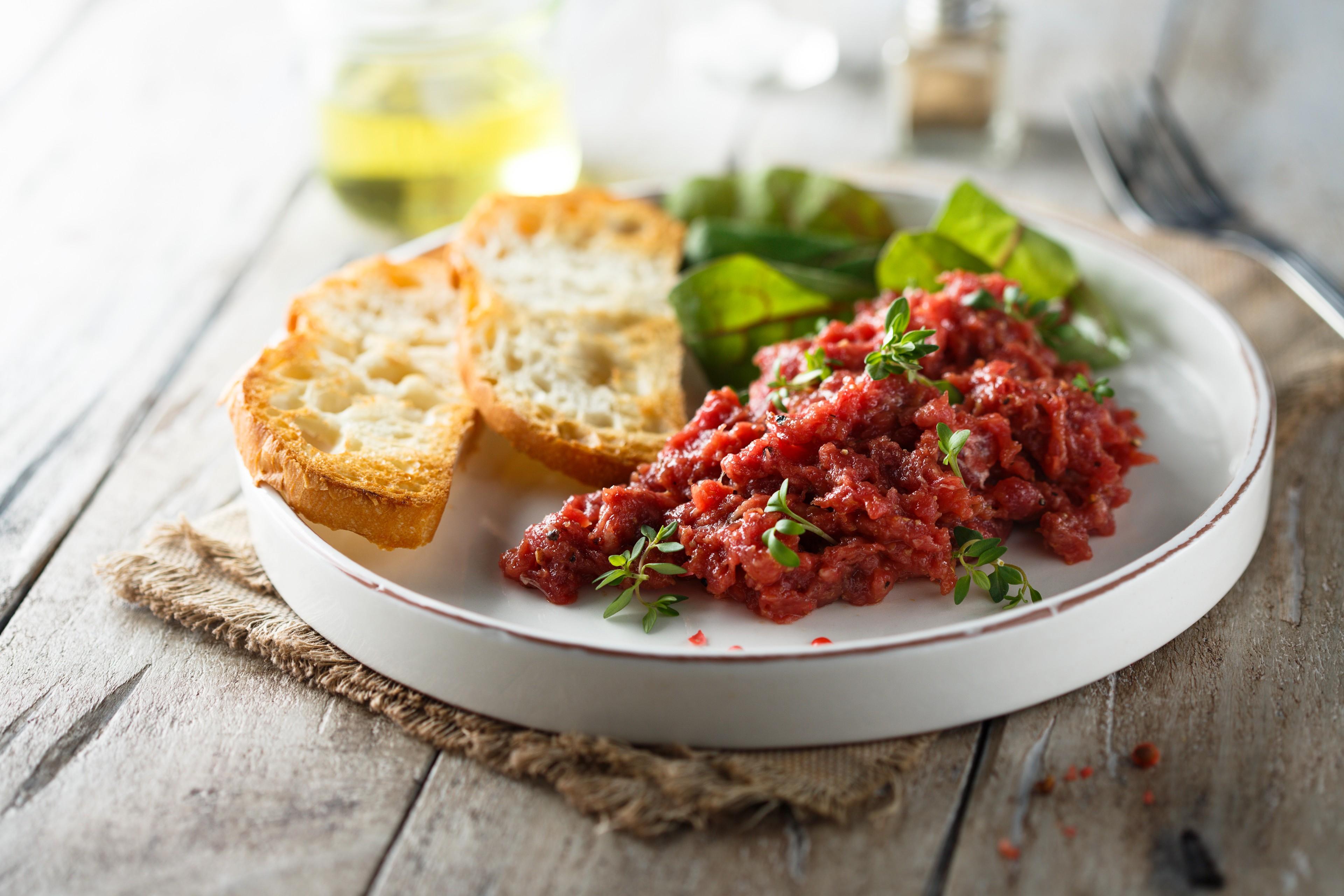 Tatar auf einem Teller mit Brotscheiben und Salat