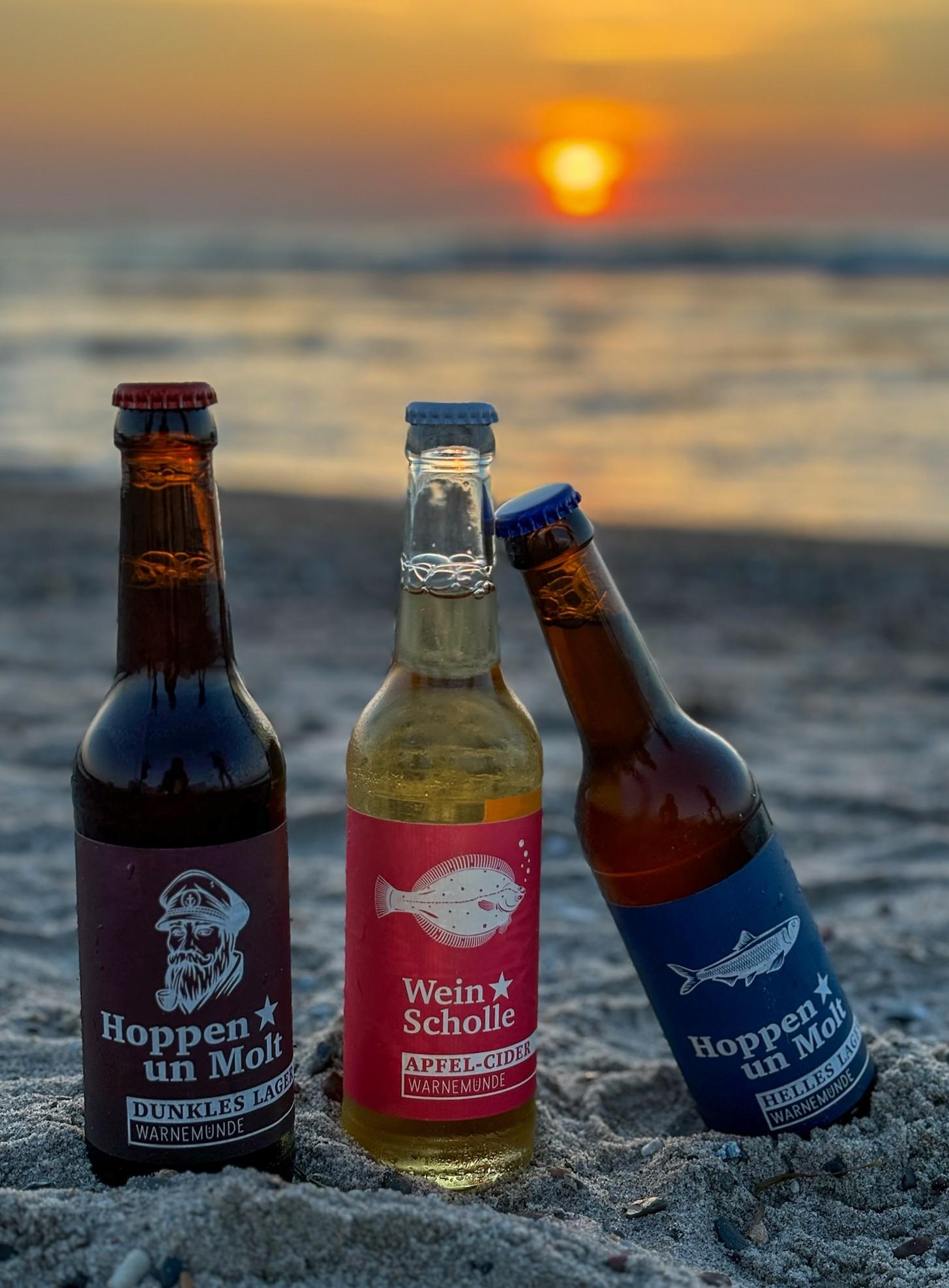 Verschiede Bierflaschen regionaler Brauereien stehen am Strand von Warnemünde