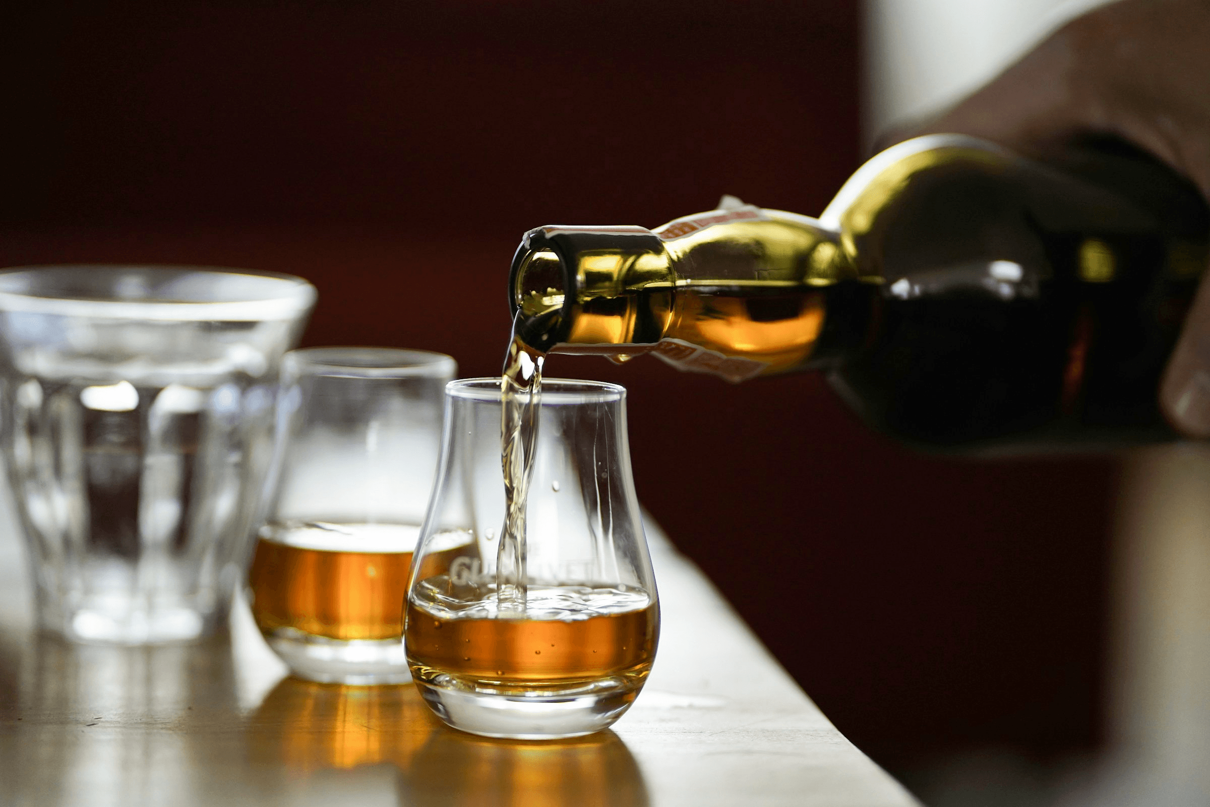 2 Whisky-Gläser auf einem Tisch, eines wird gerade befüllt