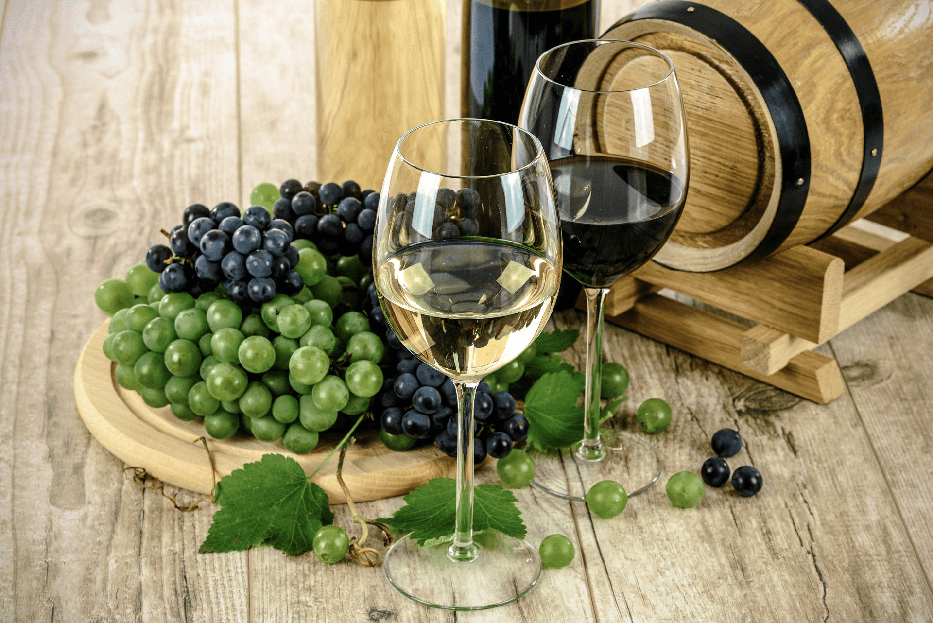 Zwei Weingläser mit Weintrauben und einem Holzfässchen im Hintergrund