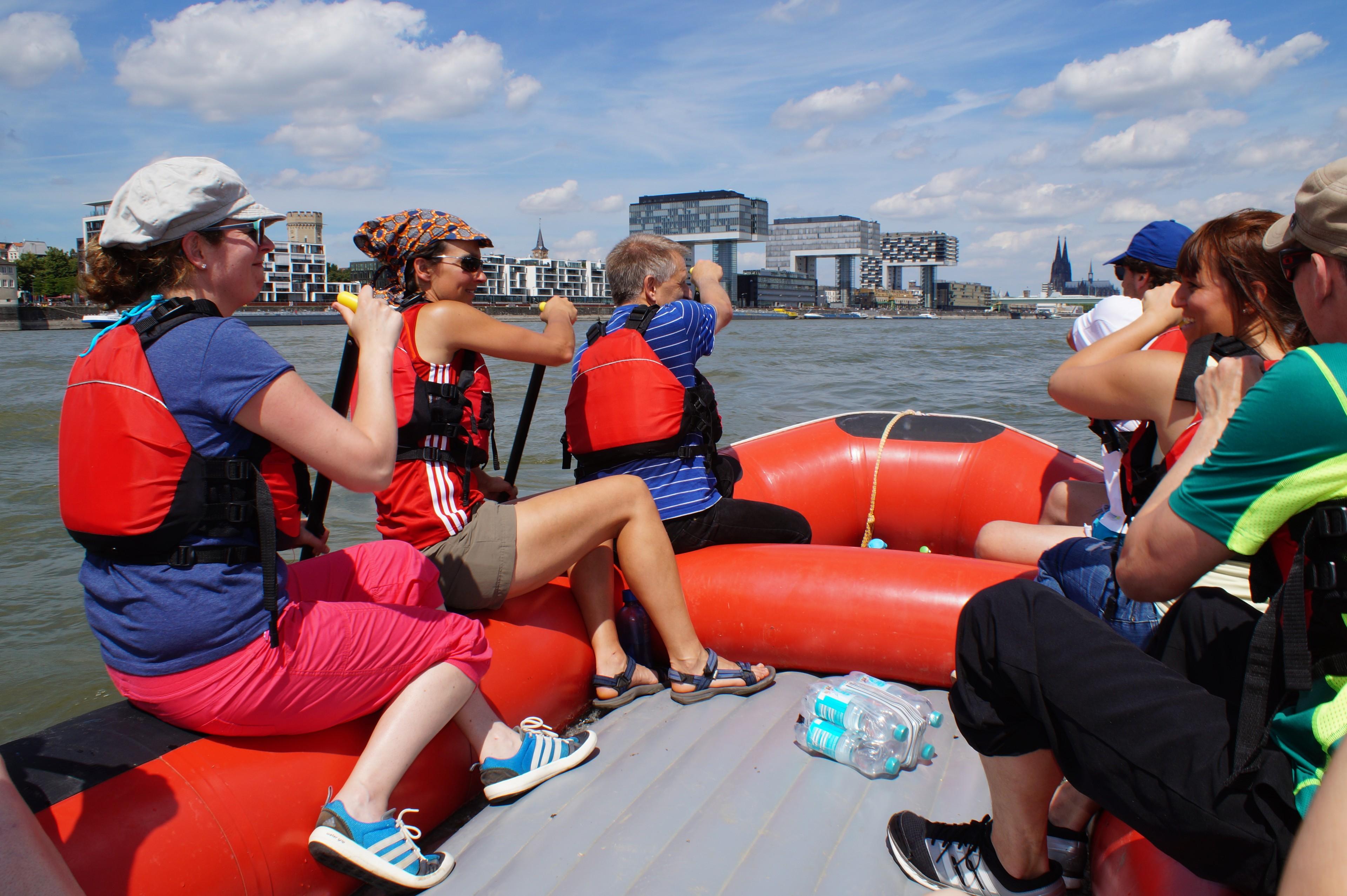 Teilnehmende einer Rafting-Tour in Köln paddeln mit einem Raft auf dem Rhein