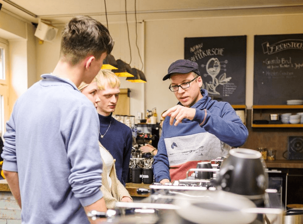 Ein Kursleiter erklärt beim Barista-Kurs das Aufschäumen der Milch